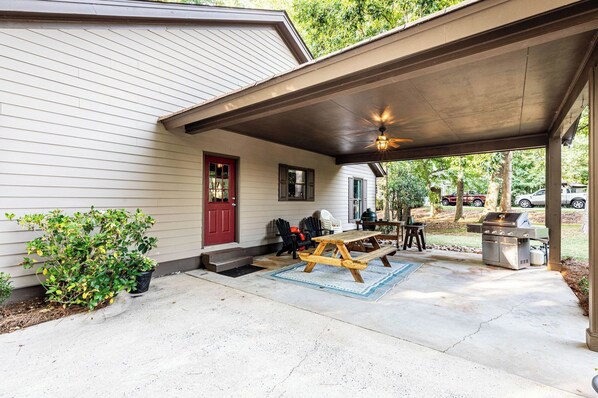A covered patio with a grill, outdoor seating, and a red door.