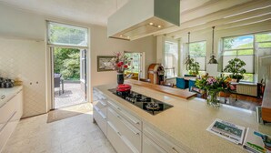 Una cocina moderna con una isla central, un comedor con mesa de madera y vistas al exterior a través de amplios ventanales.