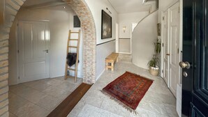 Un pasillo con un arco de ladrillo, una escalera de madera, un pequeño banco, un tapete y una planta en maceta.