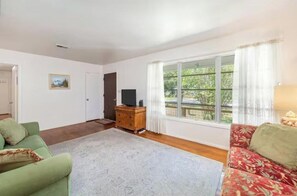 Ein Wohnzimmer mit großem Fenster, einem Fernseher auf einer Holzkommode und zwei Sofas.