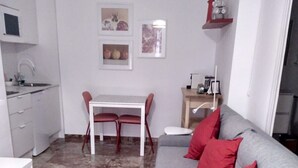 A living room with a grey sofa, red cushions, a white dining table with two chairs, a kitchen area with a sink and cabinets, and a wall with framed pictures. - Apartment 'Loft' with Shared Terrace, Wi-Fi and Air Conditioning (Córdoba)