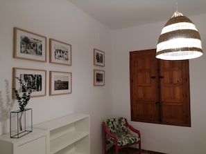 A room with a wooden door, a chair with a floral pattern, and several framed pictures on the wall.