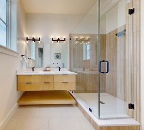 A modern bathroom with a glass shower enclosure, a double vanity with a mirror, and a wooden cabinet below.