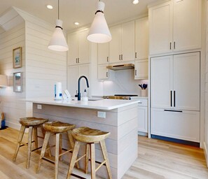 A modern kitchen with white cabinetry, a central island with stools, pendant lighting, and a built-in oven.