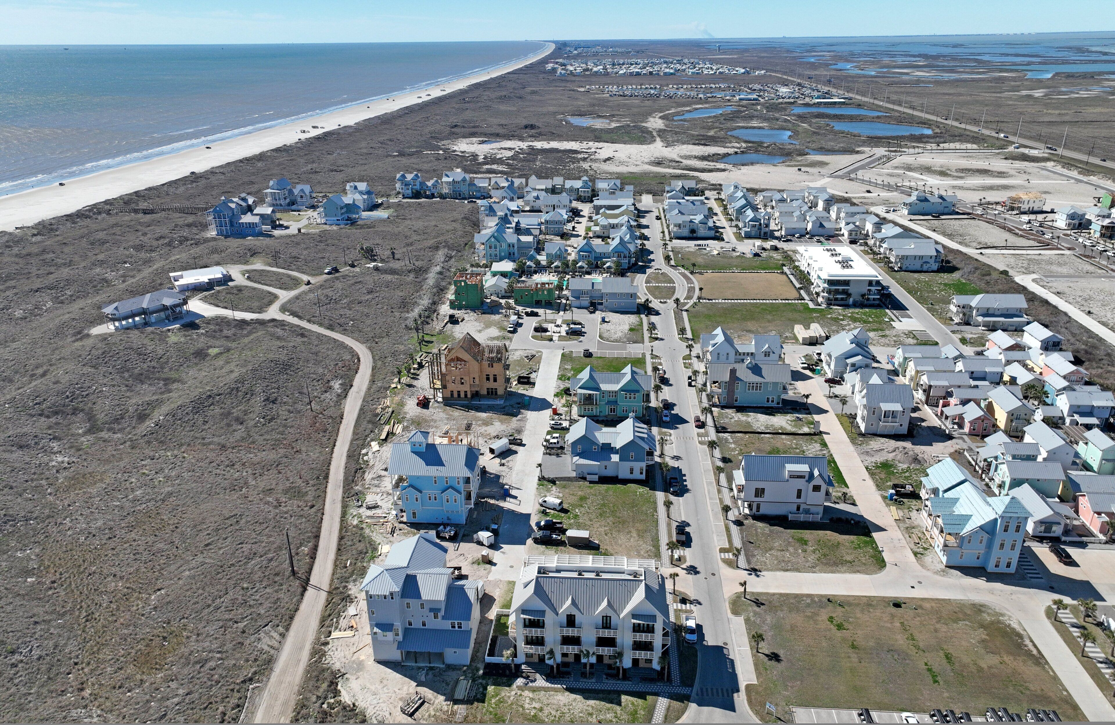 An aerial view of a coastal residential area with houses, roads, and a beach.