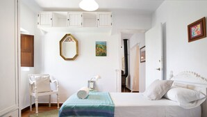 A bedroom with two beds, a chair, a dresser, a mirror, and a picture on the wall.