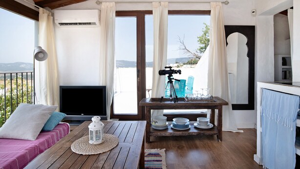 A room with a bed, a TV, a table with plates and a tripod, and a view of the outdoors.