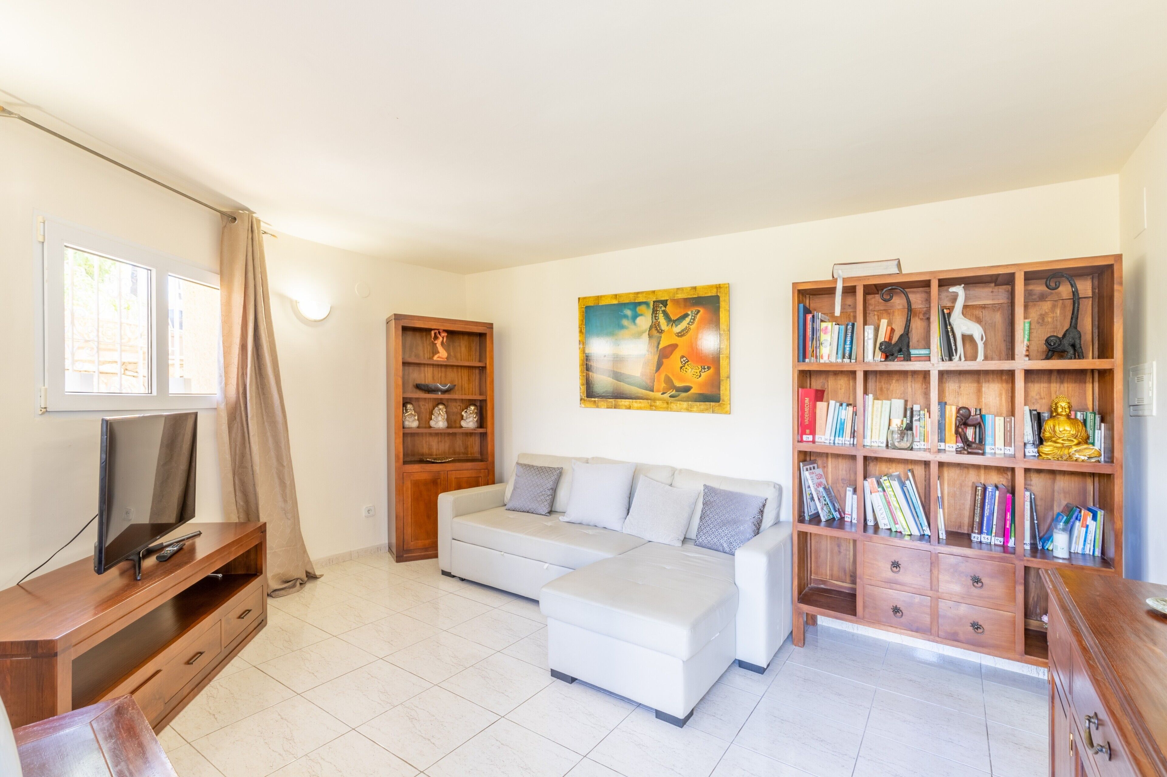A living room with a sofa, TV stand, bookshelf, and artwork.