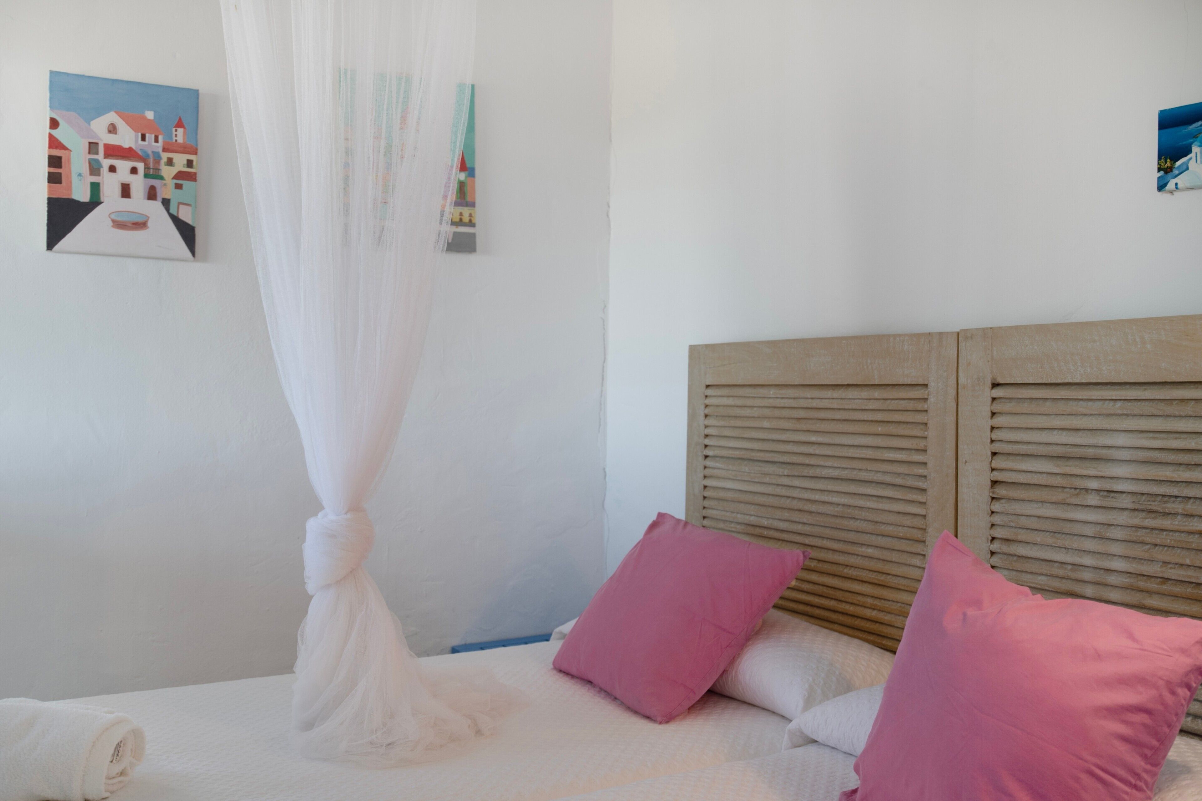 Un lit avec une tête de lit en bois, des oreillers blancs et roses, et un ciel de lit blanc.