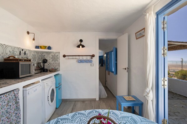 A compact kitchen with a washing machine, microwave, and a small table with a basket.