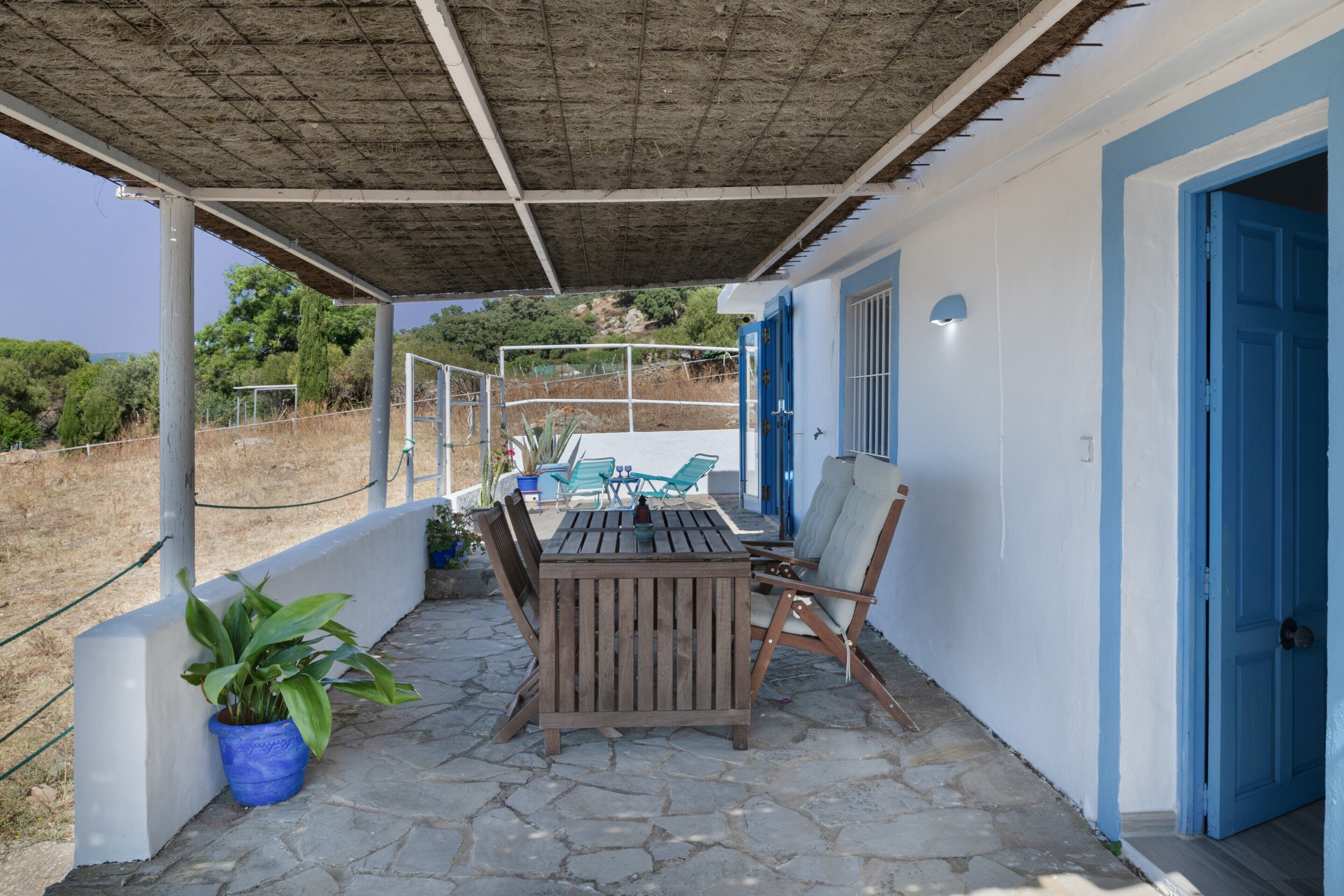 Un'area esterna riparata con tavolo e sedie, una pianta in vaso e una porta blu.