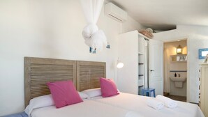 Une chambre à coucher comprenant un lit, des oreillers, une table de chevet, un baldaquin suspendu, une salle de bain avec un lavabo et un miroir.