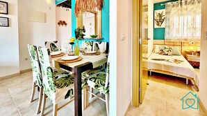 Un comedor con una mesa dispuesta para cuatro, sillas con estampado de hojas tropicales, una lámpara colgante y una pared de acento color turquesa.