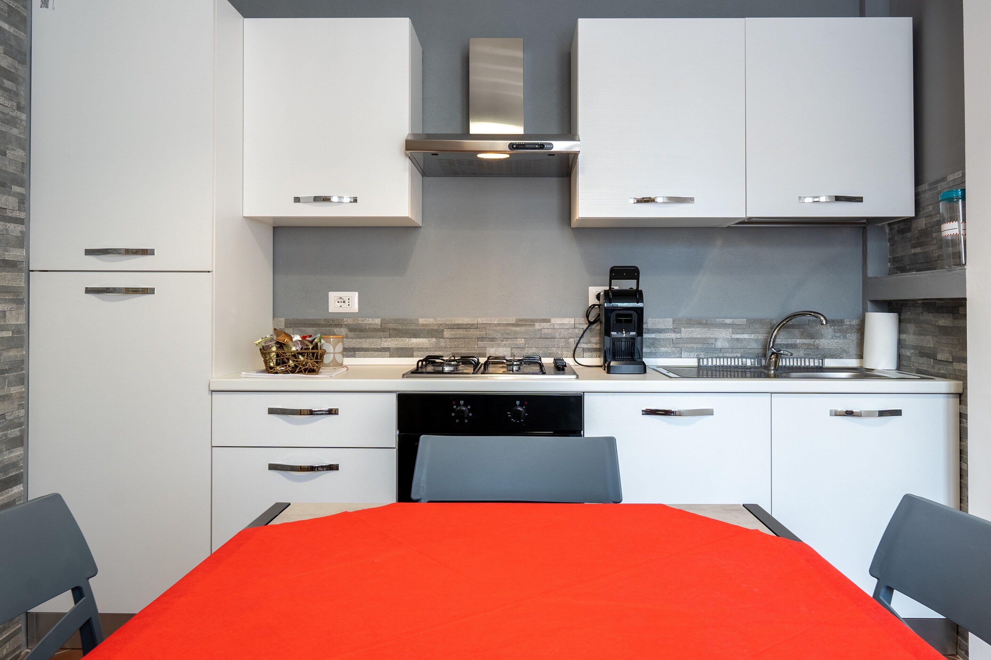 Una cucina moderna con mobili bianchi, una cappa in acciaio inossidabile, un piano cottura a gas e una macchina da caffè.