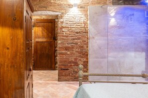 A room with a wooden door, a stone wall, and a bed with a wooden headboard. - Room 'Il Rifugio' with Wi-Fi (Foiano della Chiana)