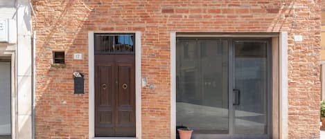 Een bakstenen gebouw met een grote glazen schuifdeur, een bruine deur en een kleine potplant.