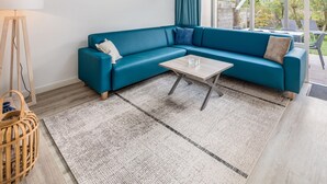 A modern living room with a teal sofa, a wooden coffee table, and a patterned rug. - Holiday Home in Oostkapelle Near the Beach (Oostkapelle)