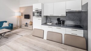 A modern kitchen with white cabinets, a built-in oven, and a sink. There is a dining area with a table and chairs. - Holiday Home in Oostkapelle Near the Beach (Oostkapelle)