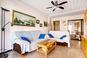 Una sala de estar con dos sofás, una mesa de centro, un ventilador de techo y un cuadro en la pared.