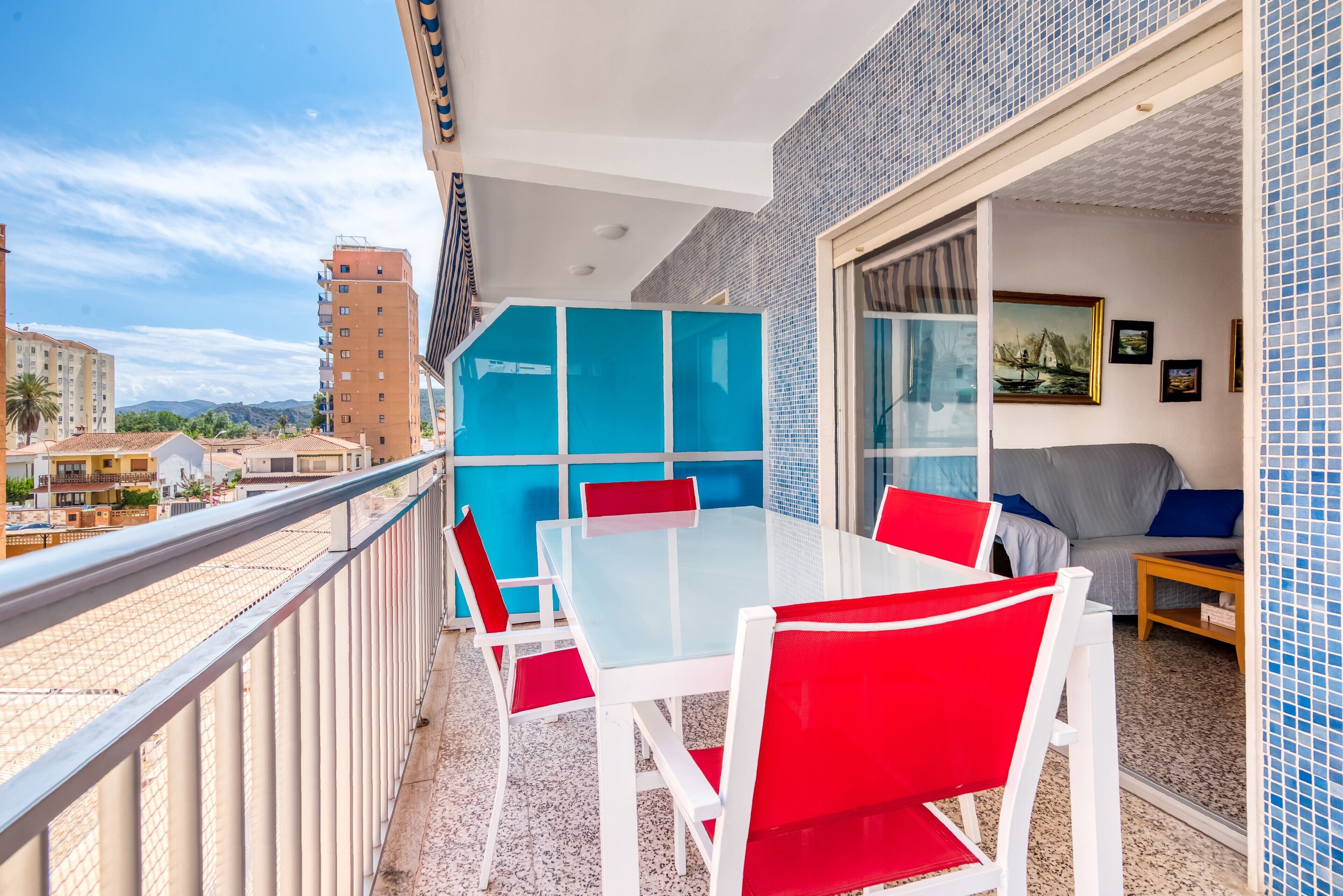 Un balcón con mesa y sillas, un sofá y vistas a edificios y montañas.