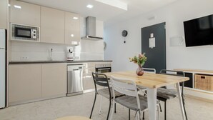 A modern kitchen with stainless steel appliances, a wooden dining table, and a flat-screen TV mounted on the wall. - Apartment 'Bellamar 4 Apartamento 2Dormitorios' with Wi-Fi and Air Conditioning (Barbate)