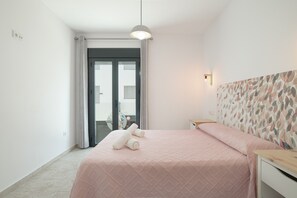 A bedroom with a bed, a bedside table, a wall-mounted light, and a view through a door.
