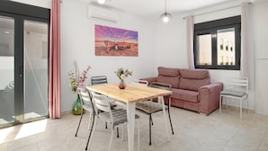 A modern living room with a dining table, sofa, and chairs, a painting on the wall, and a window with curtains. - Apartment 'Bellamar 4 Apartamento 2Dormitorios' with Wi-Fi and Air Conditioning (Barbate)