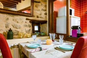 A dining table set with plates, glasses, and a cheese wheel, with stone walls and a red-tiled backsplash in the background.