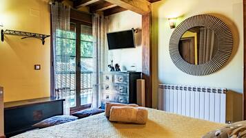 Een slaapkamer met een bed, een dressoir, een televisie, een spiegel en een raam met gordijnen.
