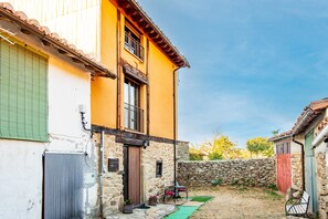 A two-story building with a stone wall, a green door, and a small patio area with a bench and potted plants.