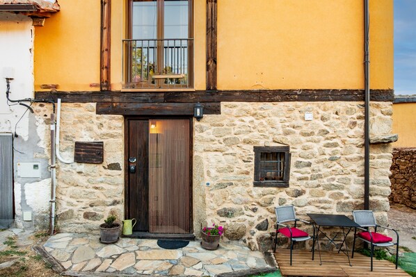 A stone building with a wooden door, a balcony, and outdoor seating.