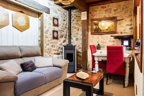 A cozy living area with a sofa, a table, a fireplace, a dining table with chairs, and a stone wall. - Country House 'Quimera' with Mountain Views, Balcony and Wi-Fi (Gil-García)