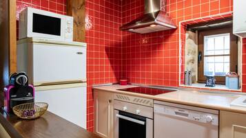 Una cocina compacta equipada con microondas, horno y lavavajillas, una encimera de madera y paredes con azulejos rojos.