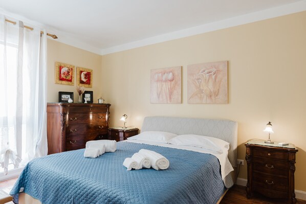 A neatly made bed with a blue quilt, a wooden dresser, and two bedside lamps.