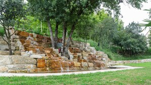A stone water feature with a cascading waterfall, surrounded by grass and trees.