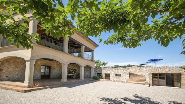 A two-story stone building with a covered patio, outdoor seating, and a stone wall with a staircase.