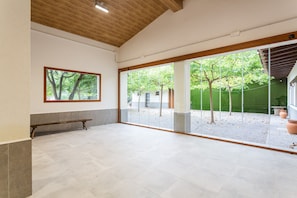 A spacious room with a large window, a wooden bench, and a framed picture on the wall.