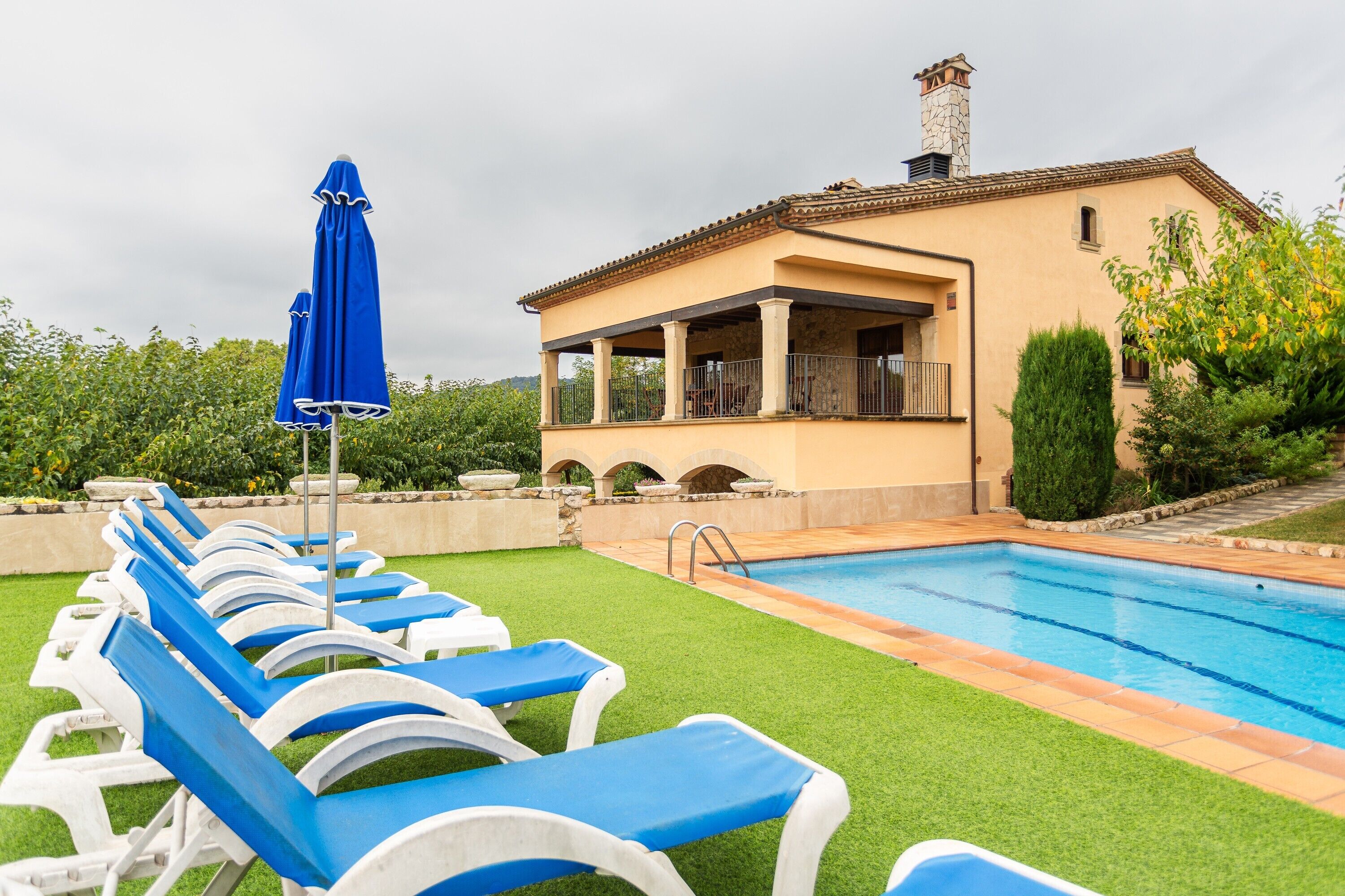 A poolside area with lounge chairs and umbrellas, a building with a tiled roof, and a clear blue pool.