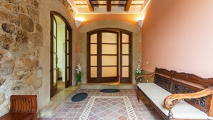 A stone-walled hallway with a wooden bench, a bench with intricate carvings, and a large arched doorway.