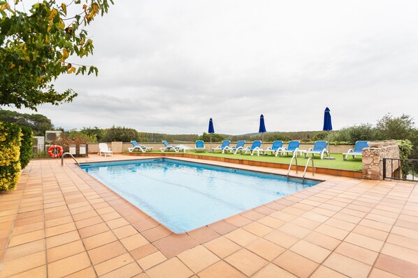 A swimming pool with blue lounge chairs and umbrellas, surrounded by greenery and a stone wall. - Country House 'Mas Vila 1' with Mountain View, Wi-Fi and Air Conditioning (Fogars de la Selva)
