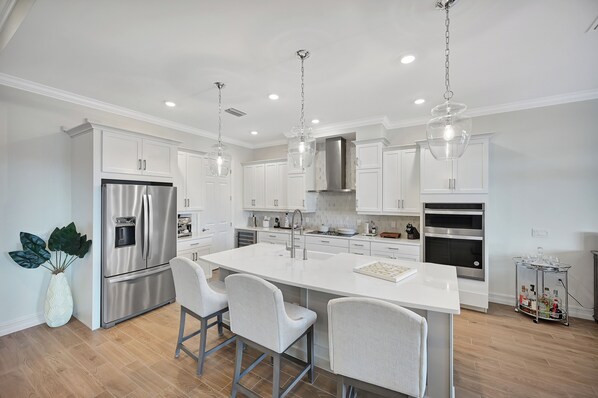 A modern kitchen with white cabinetry, stainless steel appliances, and a central island with bar stools.