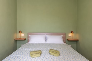 A bed with a patterned bedspread, two pillows, two bedside lamps, and two folded towels on the bed.
