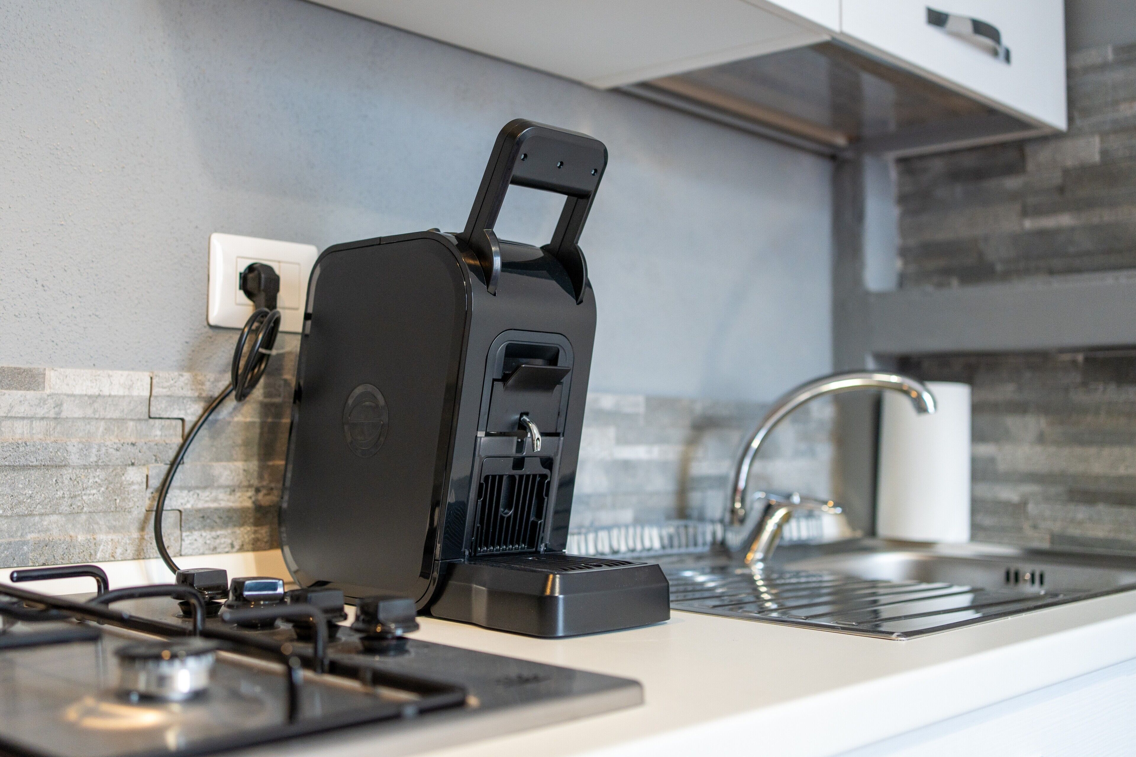 Una cucina con macchina da caffè espresso integrata, un rubinetto moderno e una parete di fondo rivestita di piastrelle.