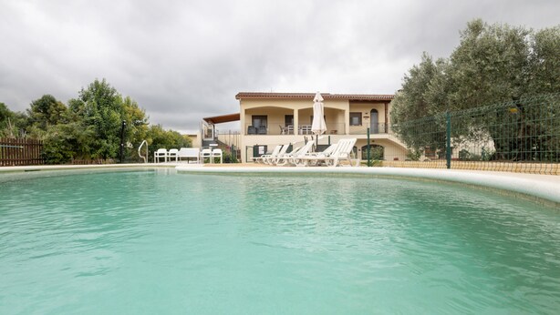 Ein Schwimmbecken mit Liegestühlen und ein Gebäude mit Balkon im Hintergrund.