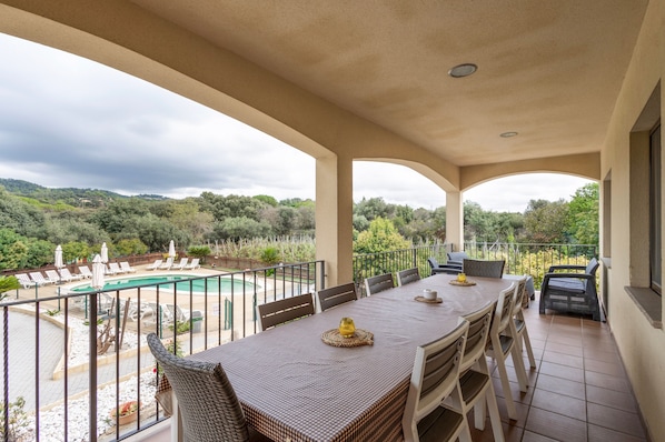 A balcony with a table and chairs, a pool, and a view of greenery.
