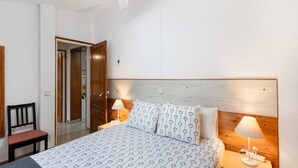 A hotel room with a bed, bedside tables, a chair, a ceiling fan, and a door leading to another room.