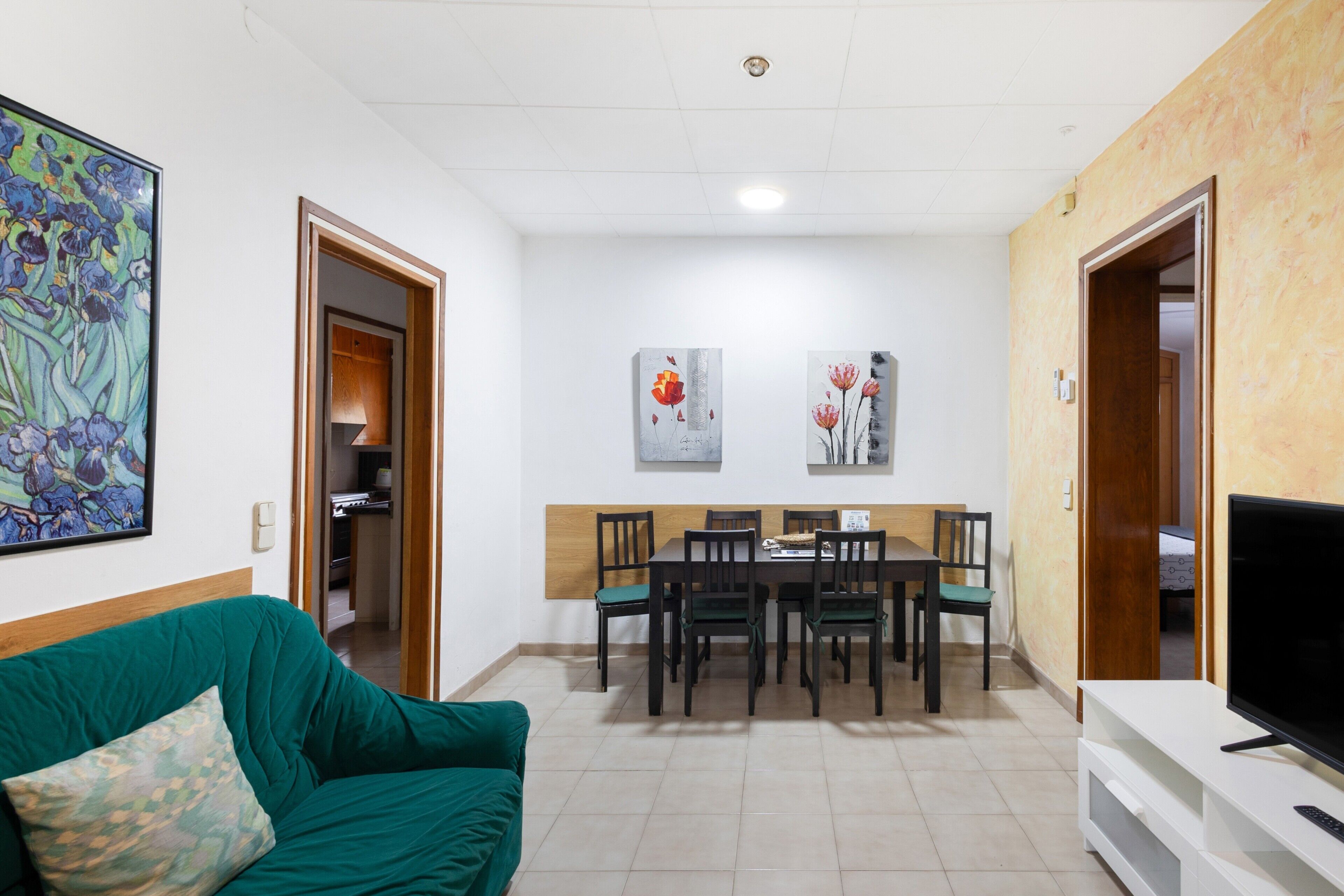 Un saló amb un sofà verd, una taula de dinar amb cadires, un televisor sobre un moble baix i obra d'art a les parets.