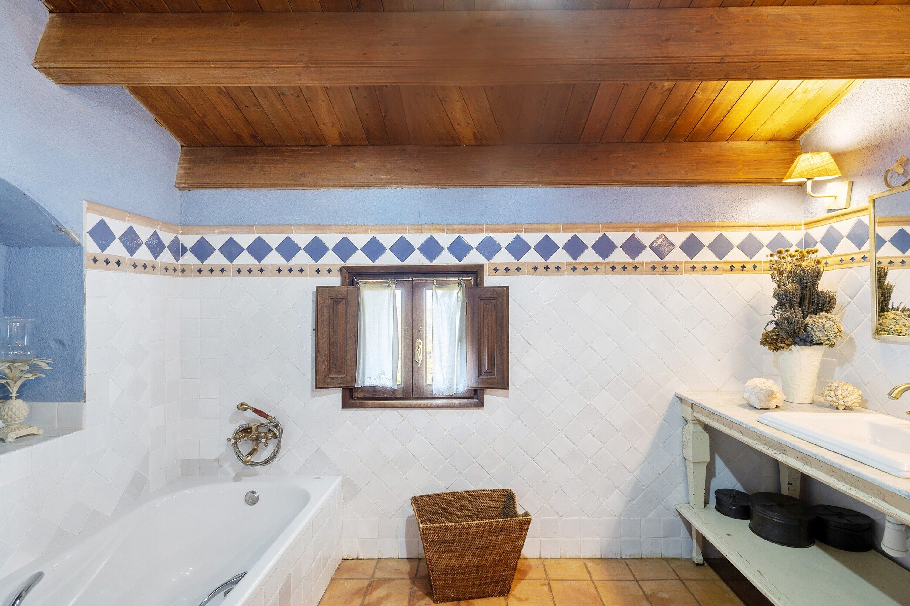 A bathroom with a bathtub, a window with curtains, a sink, and a mirror.