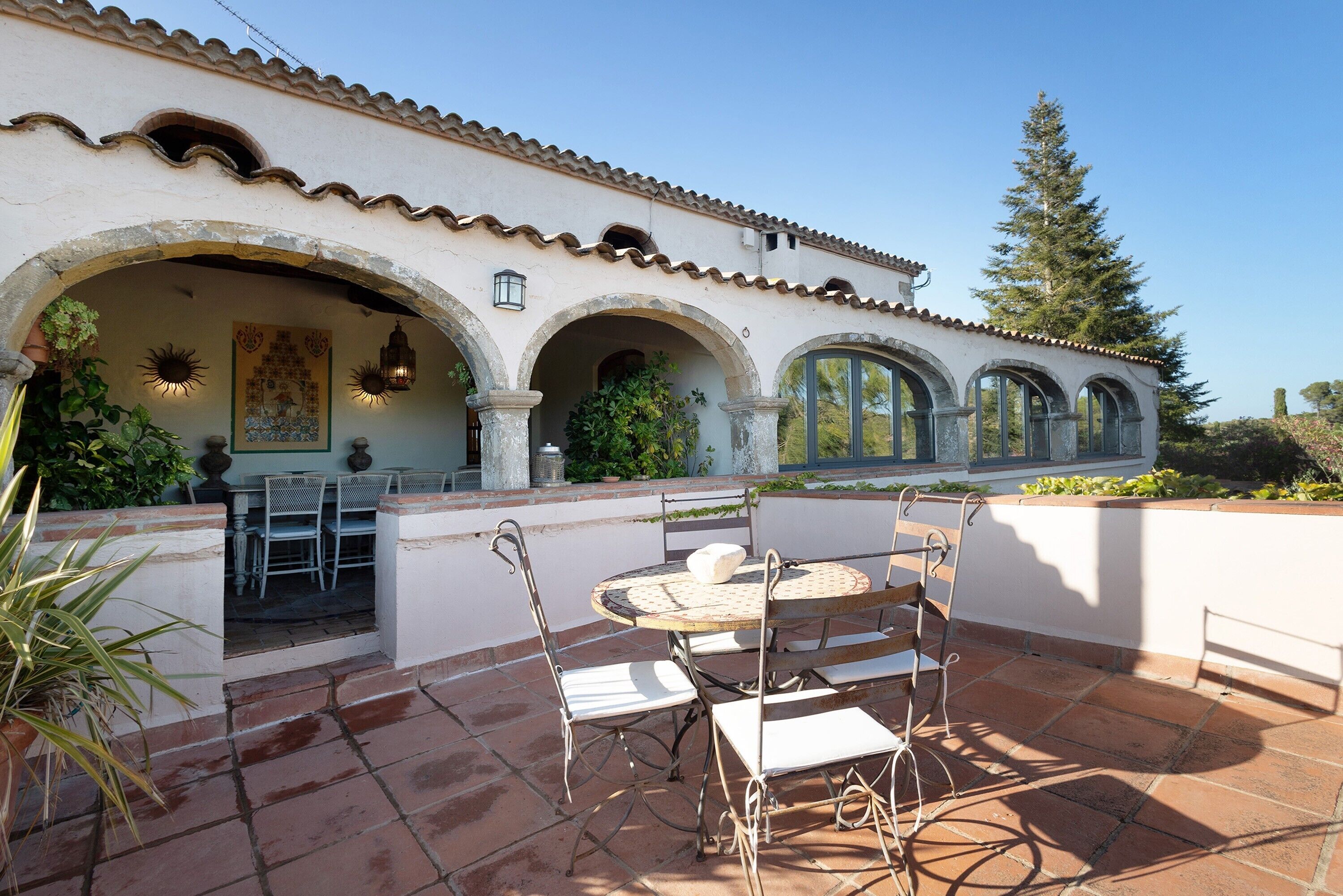 A patio with a round table and chairs, surrounded by arches and a tiled floor.