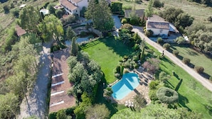 An aerial view of a property with a swimming pool, multiple buildings, and surrounding greenery.